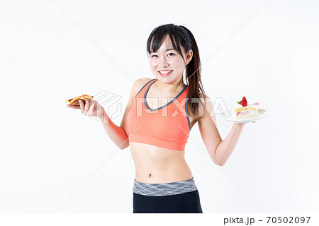 笑顔でピザとケーキを食べる筋トレ女子 糖質制限ダイエットイメージの若い女性 好きに食べるの写真素材