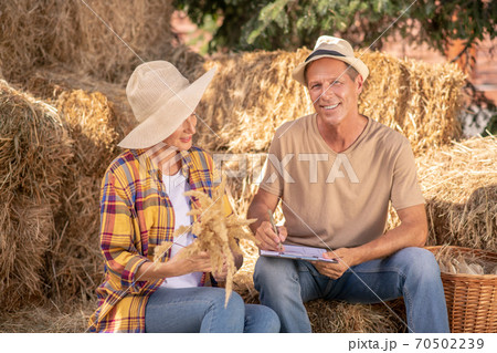 Female farmer holding millet spikelets, male sitting with clip folder, taking notes Female farmer holding millet spikelets, male sitting with clip folder, taking notes 70502239