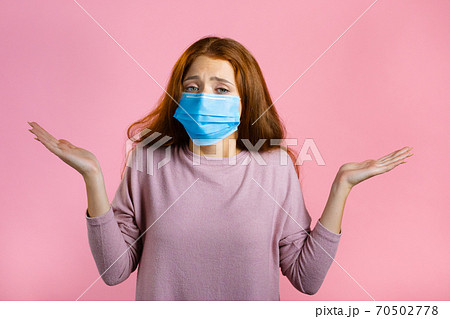 Unsure woman in medical mask shrugs her arms, makes gesture of I don't know, care, can't help Unsure woman in medical mask shrugs her arms, makes gesture of I don't know, care, can't help 70502778