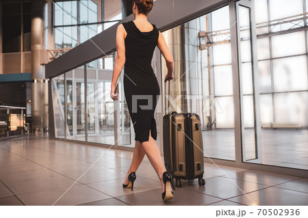 Woman wearing a black dress and carrying a suitcase 70502936