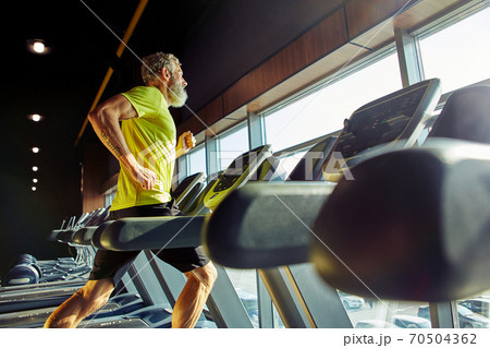 Side view of a athletic middle aged man in sportswear running on a treadmill in a gym, doing cardio before workout 70504362