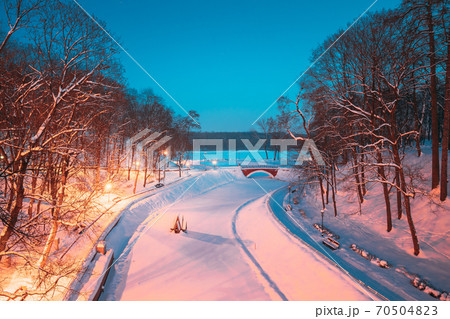 Gomel, Belarus. City Park In Winter Night. Old Bridge And Frozen Pond In Homiel Park, Belarus. Famous Local Landmark In Snow Gomel, Belarus. City Park In Winter Night. Old Bridge And Frozen Pond In Homiel Park, Belarus. Famous Local Landmark In Snow 70504823