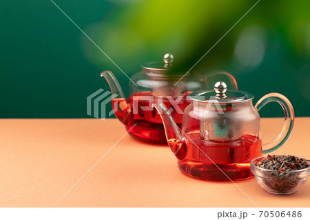 Glass teapot with black tea on background of blurred foliage Glass teapot with black tea on background of blurred foliage 70506486