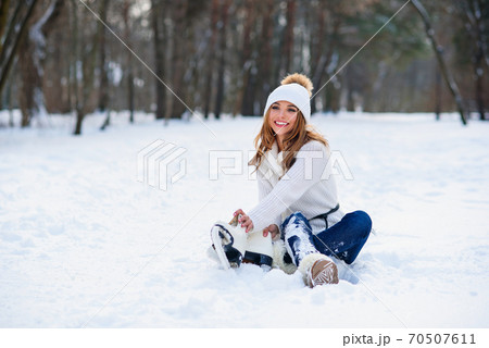 Beautiful happy woman weared in white sweater and hat with ice skates on the hands having fun in winter snowy park. Winter holidays concept. 70507611