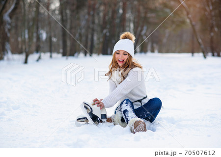 Young woman sits on the frosty snow in winter park. Winter holidays concept. 70507612