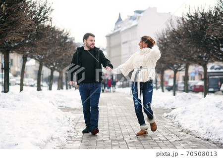 Beautiful happy girl and her handsome boyfriend walking together on the winter snowy street. New Year and Christmas concept. Beautiful happy girl and her handsome boyfriend walking together on the winter snowy street. New Year and Christmas concept. 70508013
