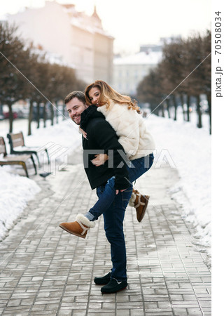 Healthy man holds his pretty girlfriend on the hands on background of winter snowy street. New Year and Christmas concept. Healthy man holds his pretty girlfriend on the hands on background of winter snowy street. New Year and Christmas concept. 70508034
