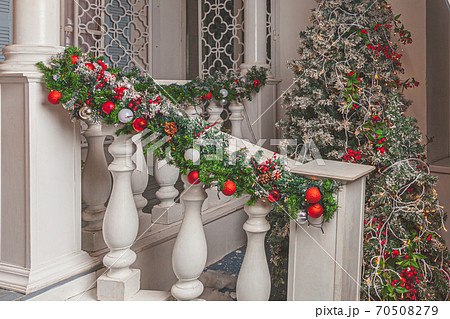 Christmas porch decoration idea. House entrance decorated for holidays. Red and green wreath garland of fir tree branches and lights on railing. Christmas eve at home 70508279