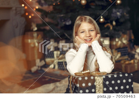 Little girl in a white sweater near christmas tree with present 70509463