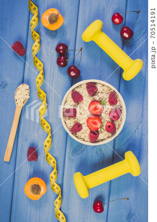 Oat flakes or oatmeal with fruits, tape measure and dumbbells 70514191