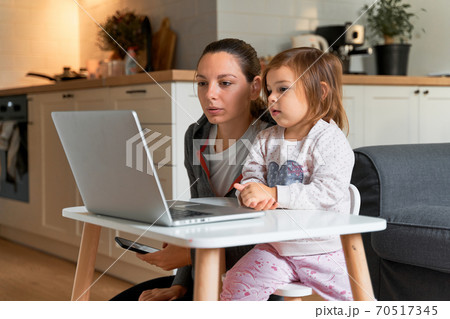 Mother and child girl sitting at home ad watching school video on laptop. Distant education 70517345