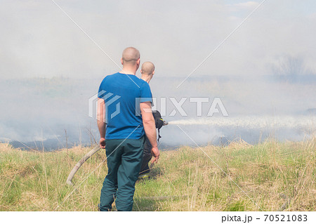 Firefighting on the field. Firefighter with a truck and a fire hose extinguishes fire.wildfire. Firefighting on the field. Firefighter with a truck and a fire hose extinguishes fire.wildfire. 70521083