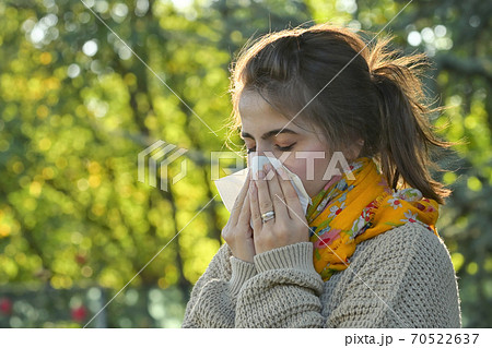 Girl in autumn park sneezing in tissue Girl in autumn park sneezing in tissue 70522637