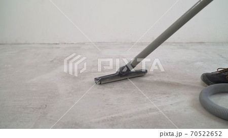 A worker is cleaning the concrete floor with a vacuum cleaner. A worker is cleaning a public concrete floor with a vacuum cleaner. Workers wear uniforms and use a blower to clean the floor. The master 70522652