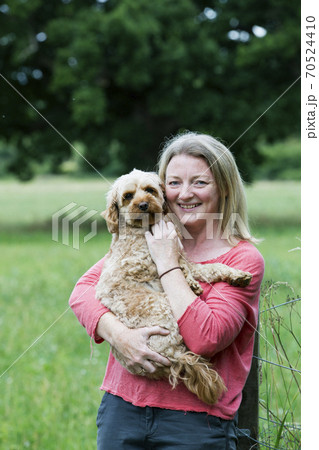 Portrait of smiling woman holding red coated young Cavapoo. 70524410
