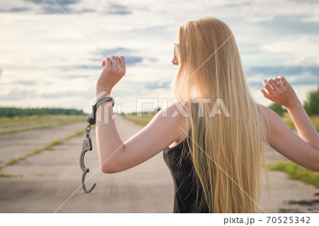 A beautiful married model girl with long hair with handcuffs on her hands is walking along an empty road to meet freedom. Family Violence	 70525342