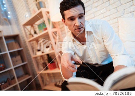 A man looks at a book while sitting at home.  70526189