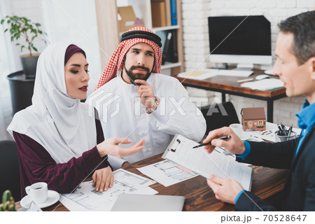 Arab couple sits at a table with a realtor. 70528647