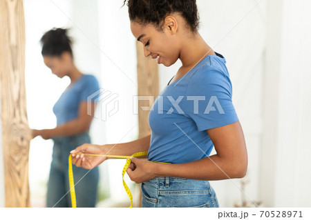 Smiling African Woman Measuring Waist After Slimming Standing At Home Smiling African Woman Measuring Waist After Slimming Standing At Home 70528971
