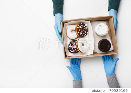 Waiter gives order during coronavirus epidemic and fast customer service. Client takes box of donuts with white and chocolate glazed and crumb and two cups of coffee takeaway 70529166