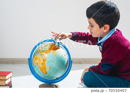 A schoolboy in a sweater sits on the floor in a pose and plays with an airplane and a globe. The illusion of travel. A schoolboy in a sweater sits on the floor in a pose and plays with an airplane and a globe. The illusion of travel. 70530407