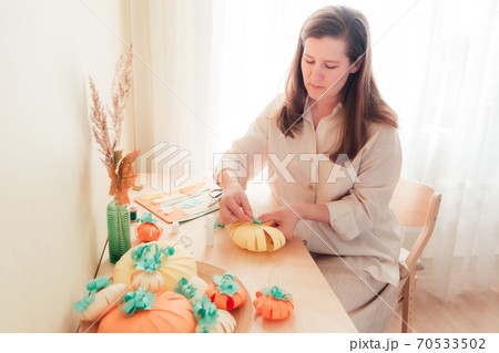 A young woman sits at a desk and makes a homemade paper pumpkin 70533502