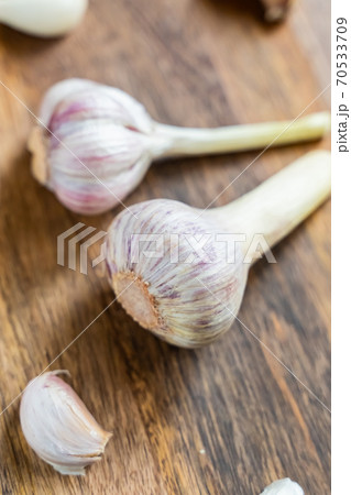 pair of garlic head in the center of scattered cloves on a wooden background 70533709