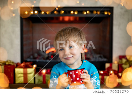 Happy child with cup of milk against fireplace 70535270