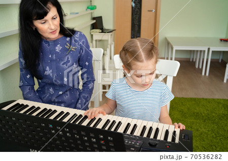 teacher teaches little girl to play on keyboard. 70536282
