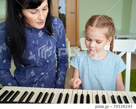 teacher teaches little girl to play on keyboard. 70536295
