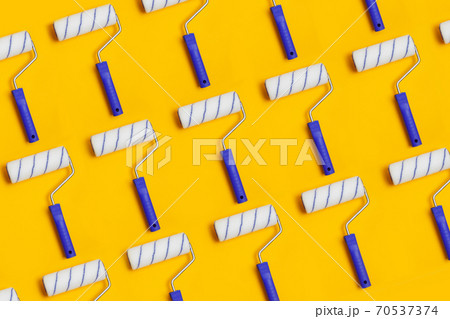 Pattern with paint roller with blue handle on yellow background. Clean roll for painting walls. Pattern with paint roller with blue handle on yellow background. Clean roll for painting walls. 70537374