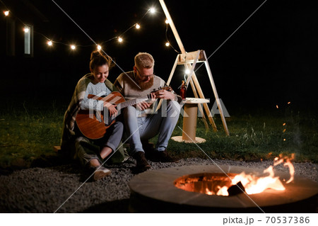Man teaching girl play a guitar on autumn night picnic Man teaching girl play a guitar on autumn night picnic 70537386