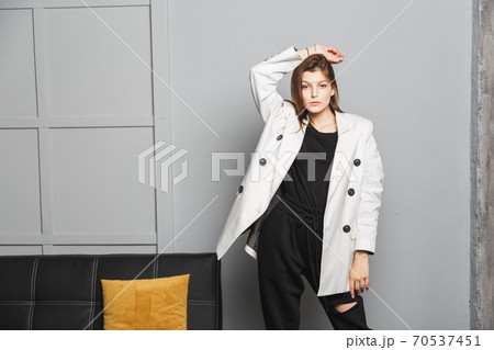 Young elegant woman in white oversize blazer and black ripped pants. Interior portrait Young elegant woman in white oversize blazer and black ripped pants. Interior portrait 70537451