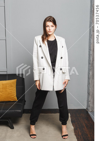 Young elegant woman in white oversize blazer and black ripped pants. Interior portrait Young elegant woman in white oversize blazer and black ripped pants. Interior portrait 70537456