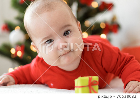 merry christmas christmas and happy new year, infants, childhood, holidays concept - close-up 6 month old newborn baby in red clothers on his tummy crawls with decorations gifts near christmas tree. 70538032