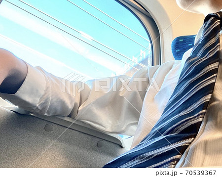 新幹線移動の出張中にビジネススーツを脱ぎワイシャツ姿で一息つく男性 70539367