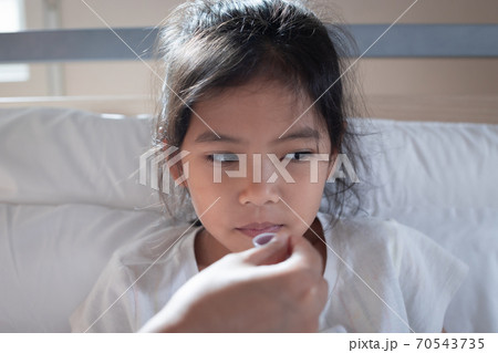 Asian mother giving cough syrup medicine on a spoon to her daughter in bed, Sick child and health care concept. 70543735