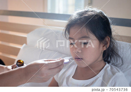 Asian mother giving cough syrup medicine on a spoon to her daughter in bed, Sick child and health care concept. 70543736