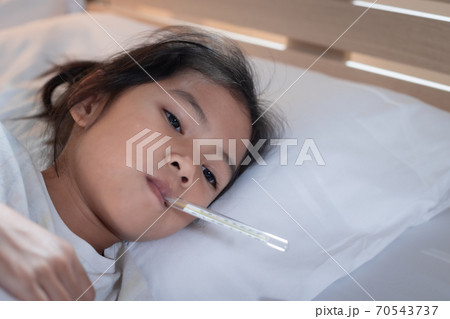 Sick asian child girl is sleeping on bed and measuring her body temperature with thermometer in the bedroom at home. Sick asian child girl is sleeping on bed and measuring her body temperature with thermometer in the bedroom at home. 70543737