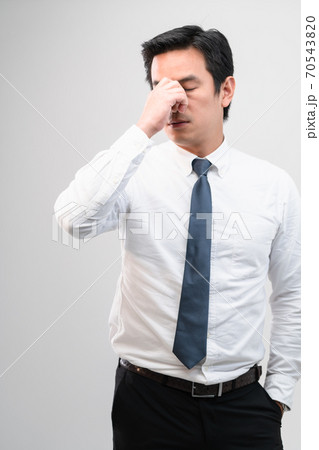 Exhausted Asian worker Squeezing between the eyebrows to try relaxing from hard work shows pain expression face, concept working exhausted, office worker lifestyle, office syndrome, tiring work hour. Exhausted Asian worker Squeezing between the eyebrows to try relaxing from hard work shows pain expression face, concept working exhausted, office worker lifestyle, office syndrome, tiring work hour. 70543820