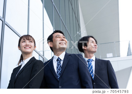 ビルの前で立つ3人の笑顔のビジネスパーソン ビルの前で立つ3人の笑顔のビジネスパーソン 70545793