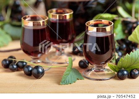 Homemade black currant liqueur and fresh berries . 70547452