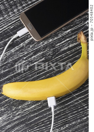 Touchscreen smartphone is connected to a fresh juicy banana with a white usb cable. The concept of measuring the useful properties and qualities of food using a mobile application 70548402