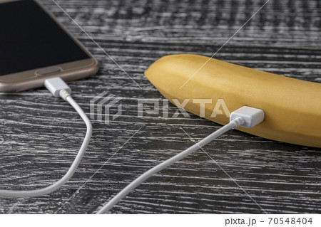 Touchscreen smartphone is connected to a fresh juicy banana with a white usb cable. The concept of measuring the useful properties and qualities of food using a mobile application 70548404
