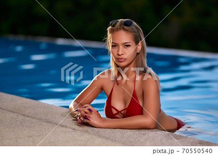 Young asian woman in red swimsuit posing at swimming pool 70550540