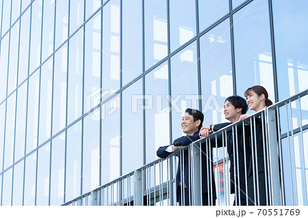 ビルの前で外を眺める3人の笑顔のビジネスパーソン ビルの前で外を眺める3人の笑顔のビジネスパーソン 70551769