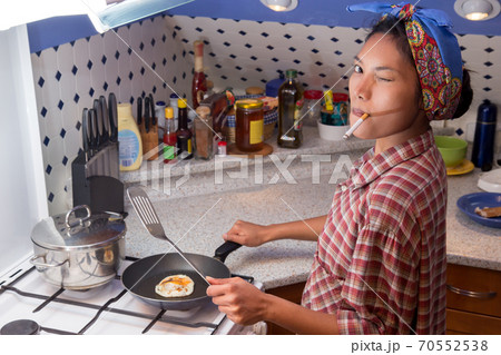 A young woman smokes a cigarette and cooks in the kitchen 70552538