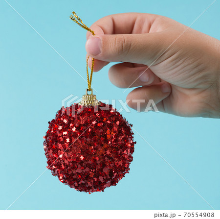 child's hand holds a Christmas tree toy, red decorative ball, on a turquoise pastel background, christmas concept 70554908