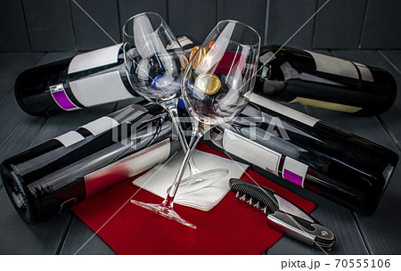 Wine glasses lying on several bottles of red wine and a corkscrew, on red tablecloth in wooden table Wine glasses lying on several bottles of red wine and a corkscrew, on red tablecloth in wooden table 70555106