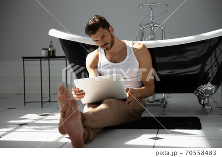 Man with laptop sitting near bath 70558483